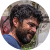 Homme souriant en extérieur, mur en arrière-plan.