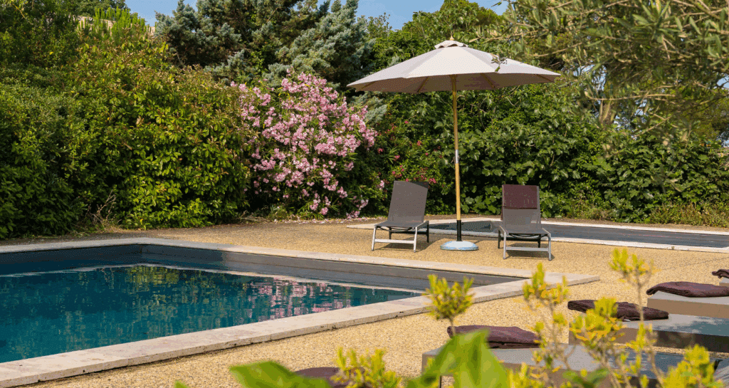 Piscine extérieure avec chaises longues et parasol.