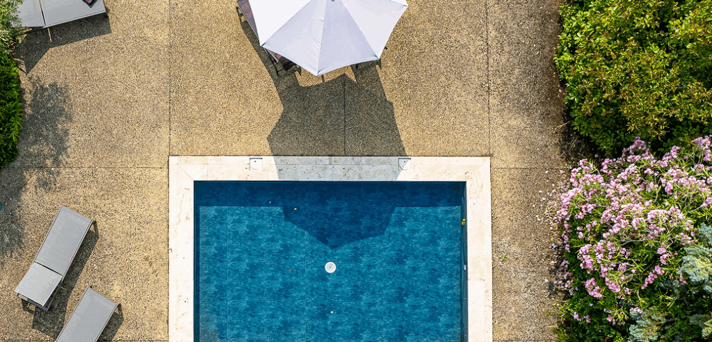 Vue aérienne piscine, parasol, transats et fleurs.